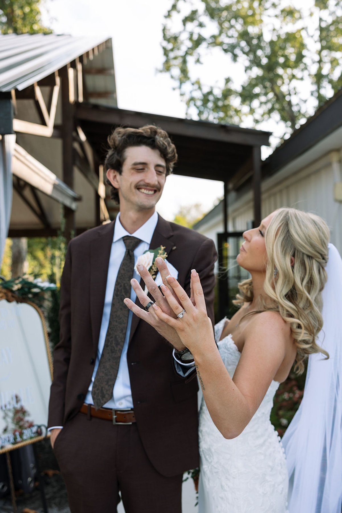 Bride showing wedding ring while smiling at groom outdoors