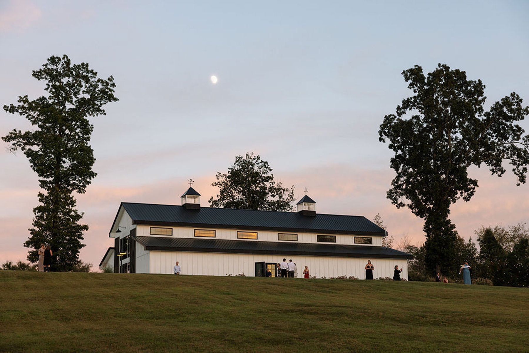White barn wedding venue exterior at sunset with guests gathering