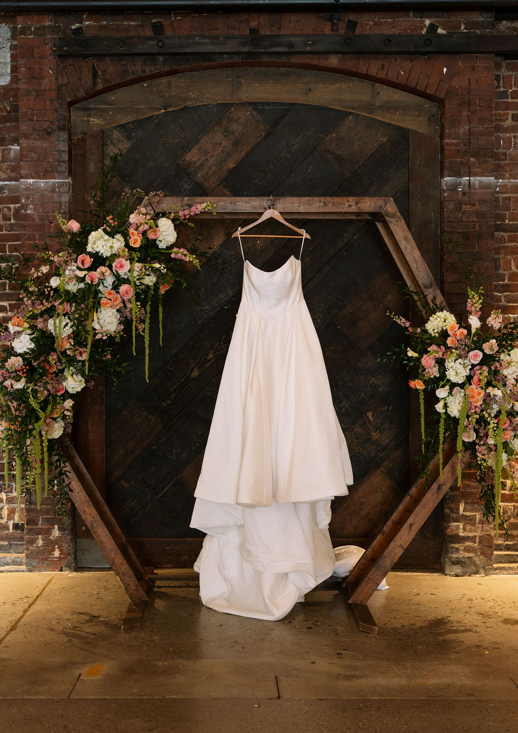 Wedding dress hanging in front of dark wood doors and floral installations at Jackson Terminal Knoxville