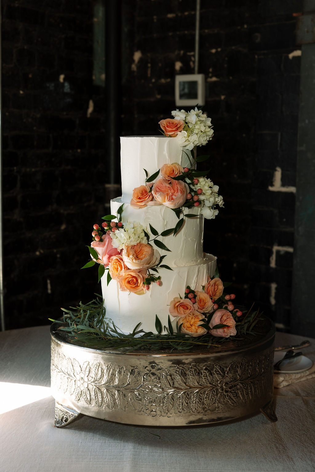 Three-tier wedding cake with floral decorations on silver stand at reception