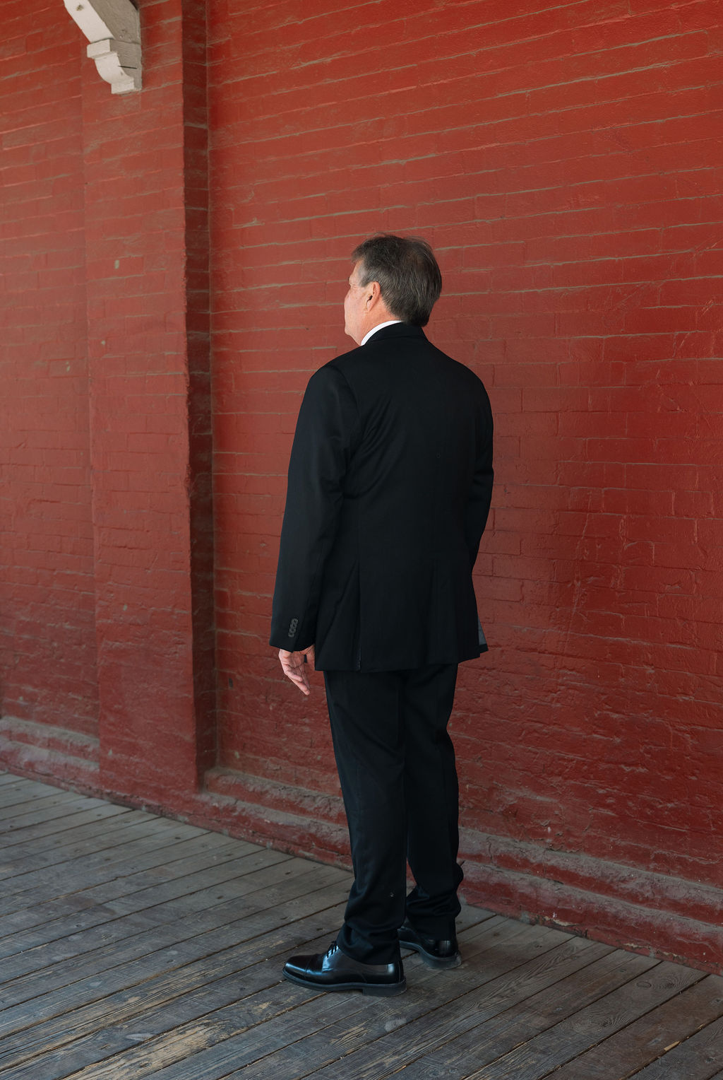 Father of the bride waiting during first look against brick wall at Jackson Terminal Knoxville