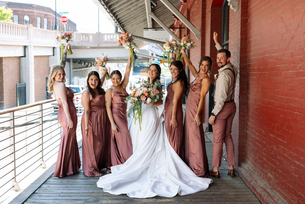 Wedding party celebrating with raised bouquets on a covered walkway at Jackson Terminal Knoxville