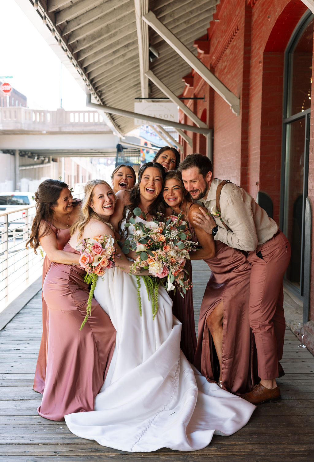 Wedding party laughing together on a covered brick walkway in downtown Knoxville, celebrating with the bride