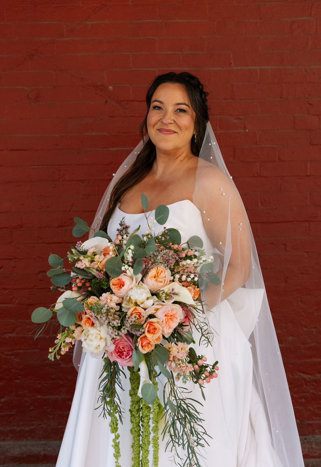Bride portrait holding bouquet with veil against red brick wall at Jackson Terminal Knoxville