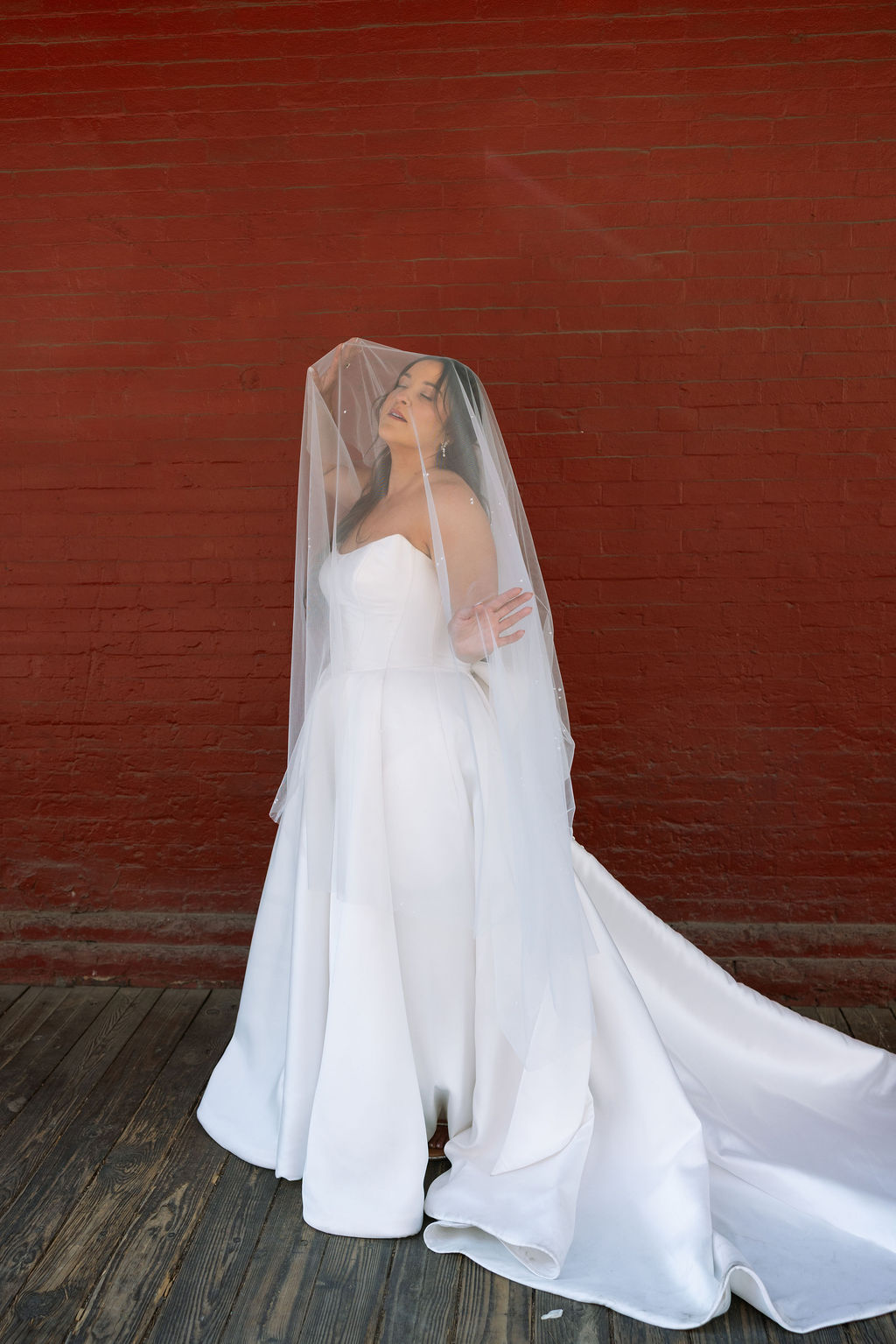 Bride portrait with veil over her face against red brick wall at Jackson Terminal