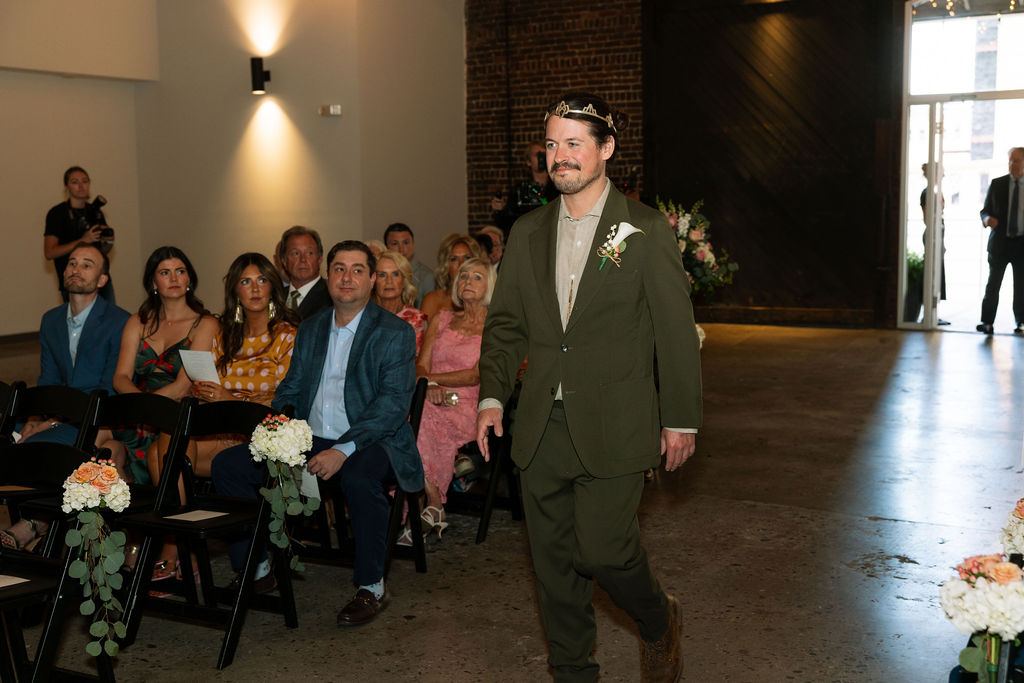 Groom walking down the aisle during indoor ceremony with guests seated on both sides