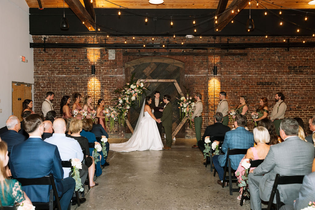 Indoor wedding ceremony at Jackson Terminal Knoxville with exposed brick walls, string lights, and floral arch