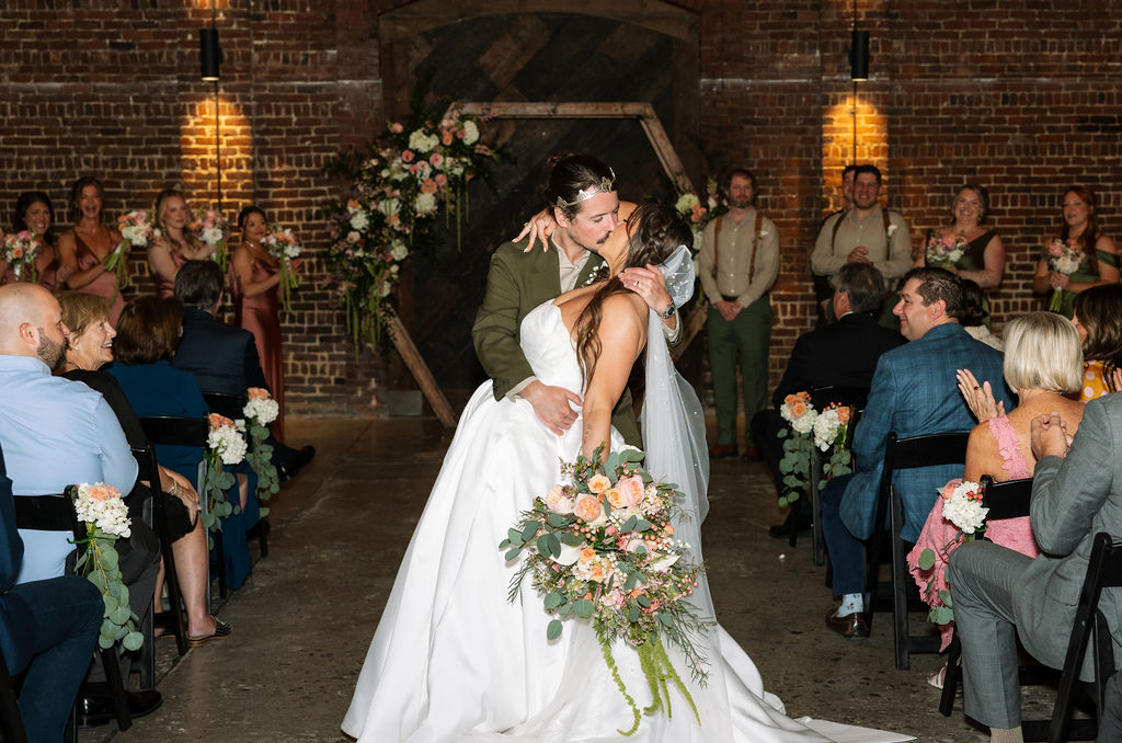 Bride and groom kissing during ceremony at Jackson Terminal Knoxville with guests celebrating around them