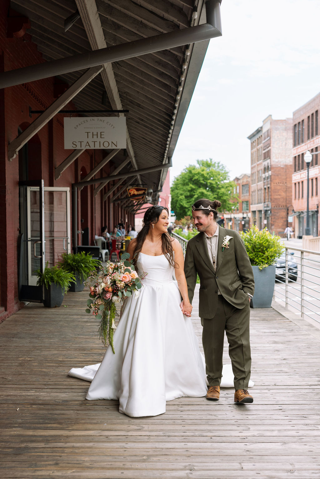Bride and groom walking hand in hand outside Jackson Terminal Knoxville with historic brick buildings and greenery