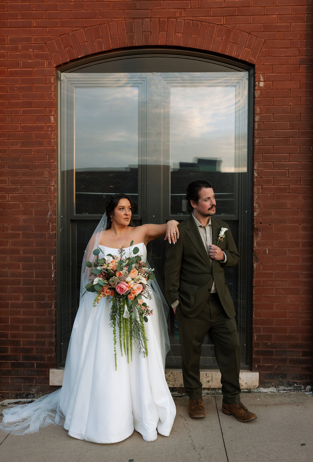 Bride and groom posing together against brick building in downtown Knoxville with dramatic lighting