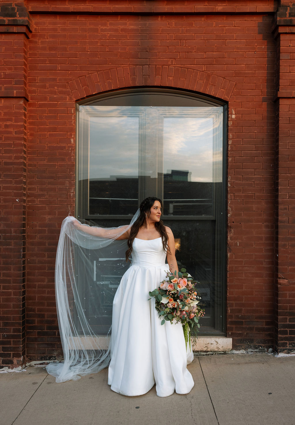 Bride portrait holding veil and bouquet in front of brick building in downtown Knoxville