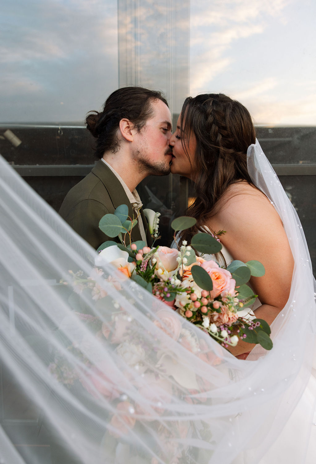 Close-up of bride and groom kissing with bouquet and veil framing the moment
