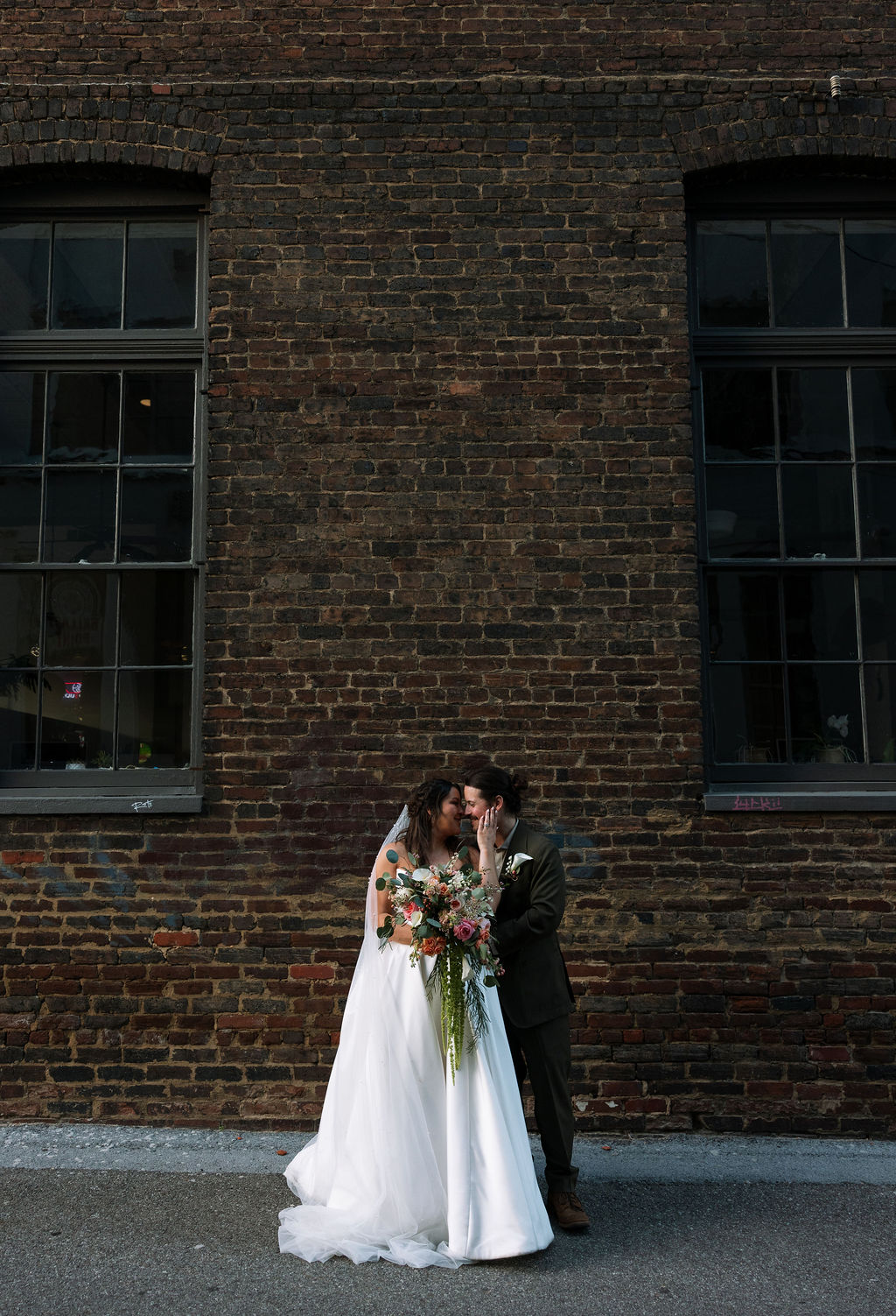 Bride and groom embracing in front of textured brick wall in downtown Knoxville