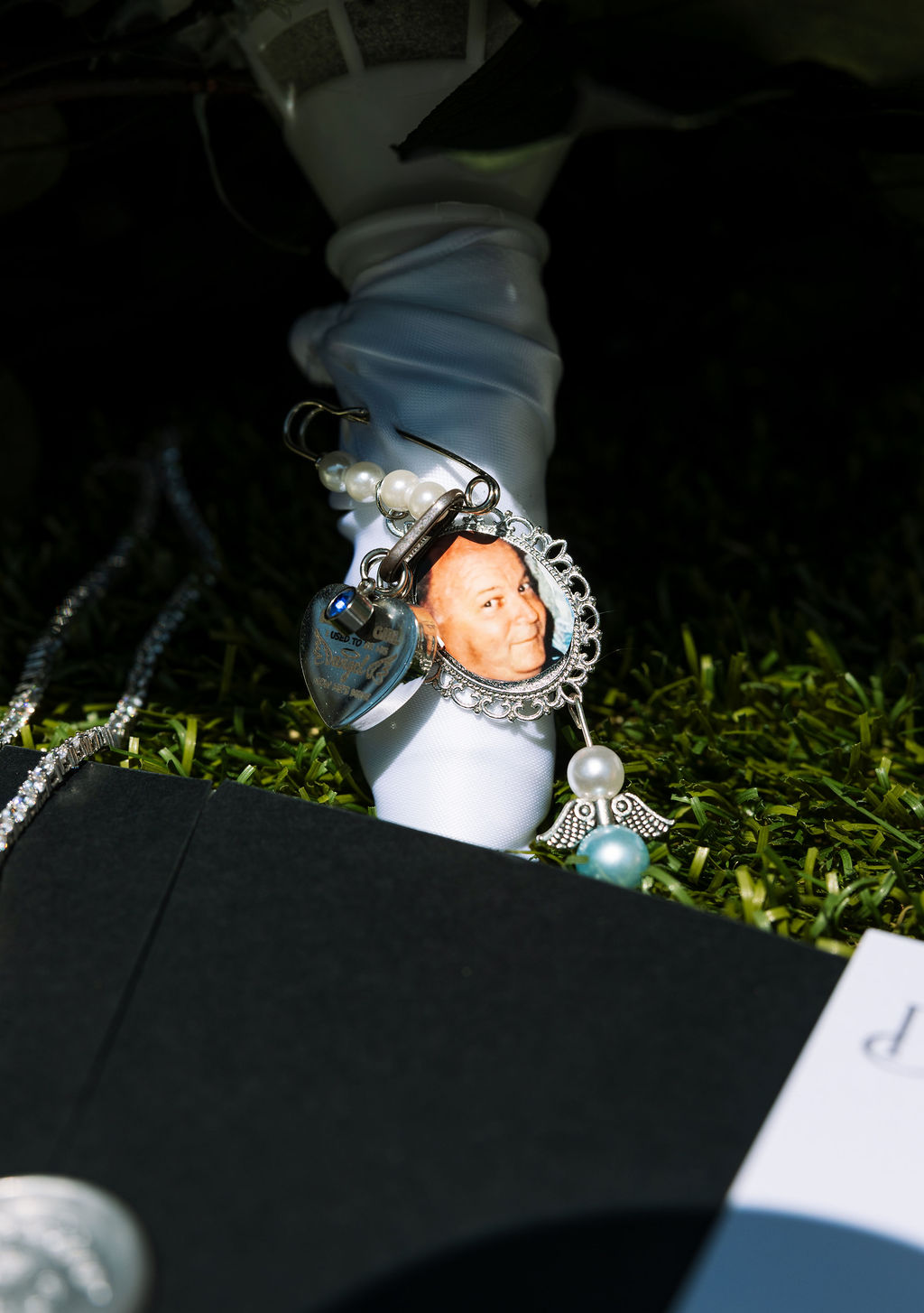Memorial photo charm attached to bridal bouquet, meaningful wedding detail photographed up close