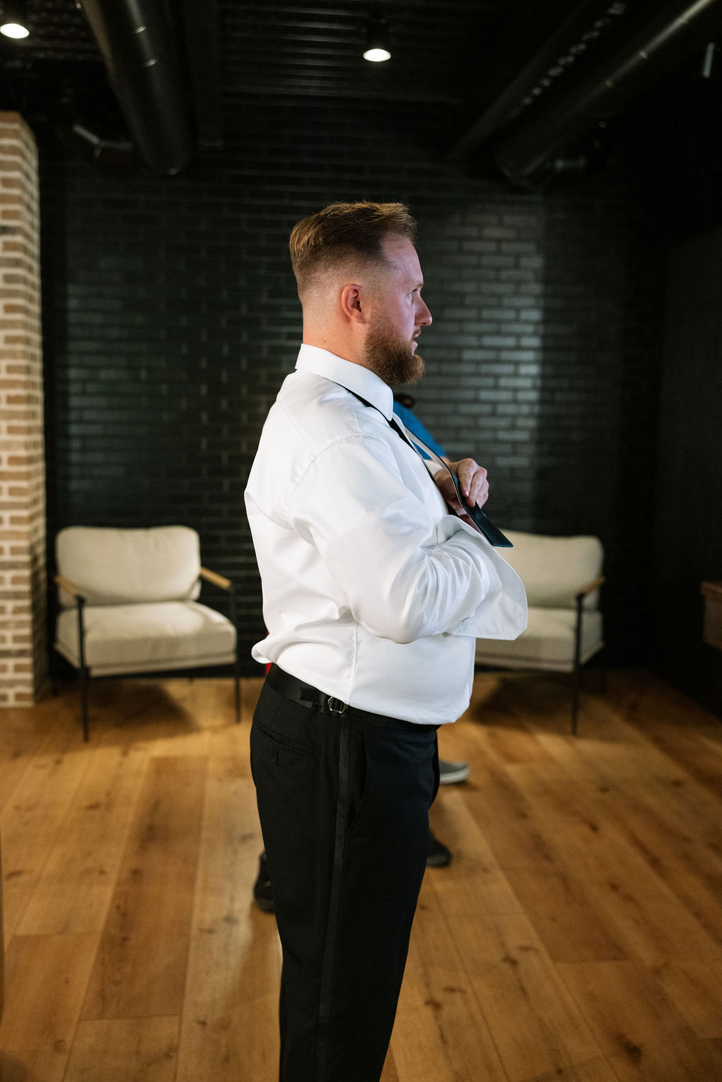 Groom adjusting tie in modern getting ready space before ceremony