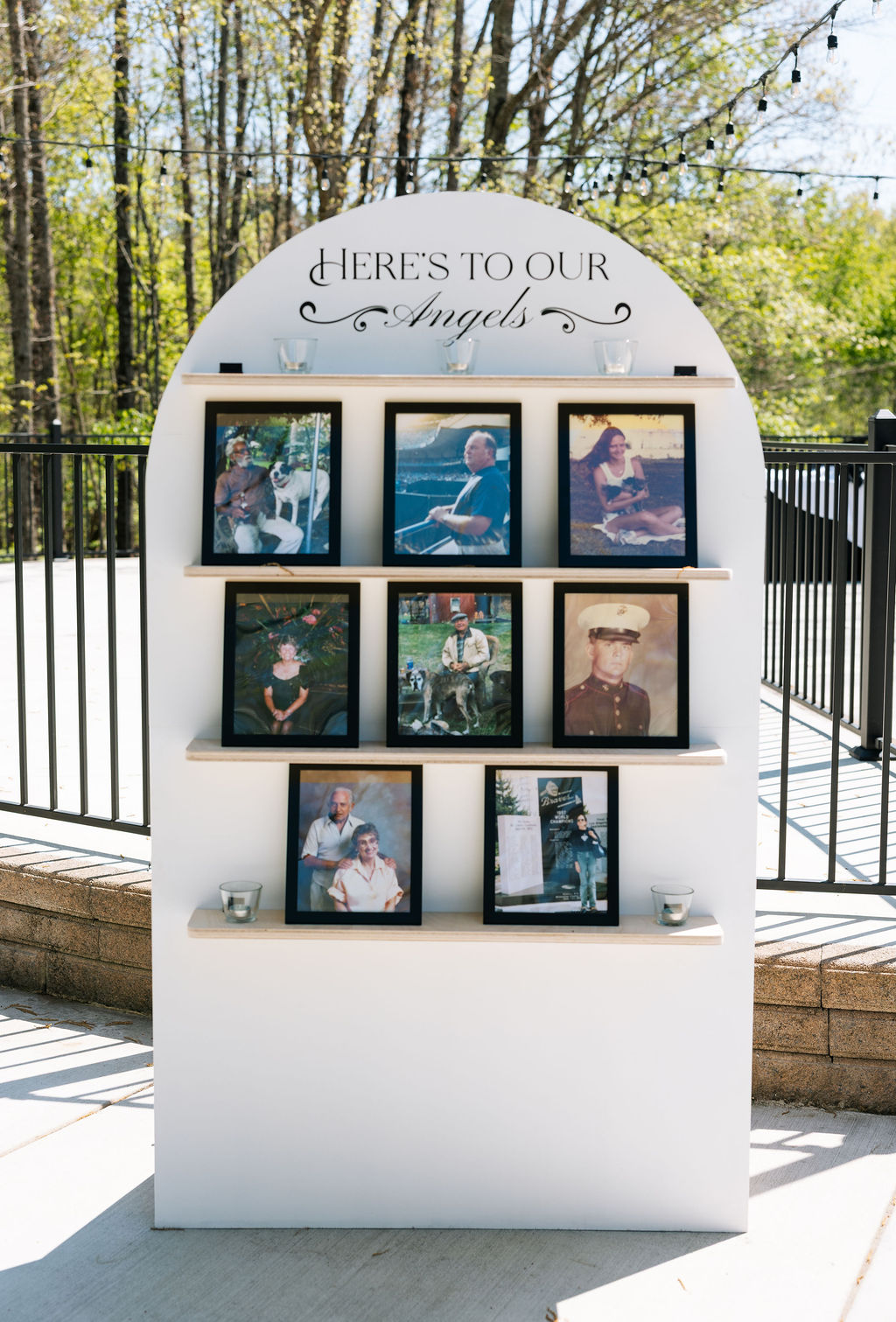 Memorial display with framed photos and “here’s to our angels” sign at outdoor reception