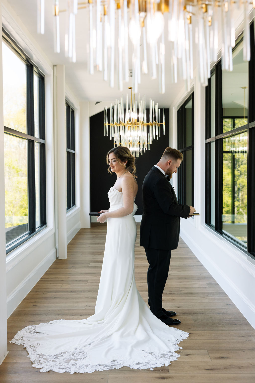 Bride and groom back to back in modern hallway space with chandeliers during a nichols heir wedding