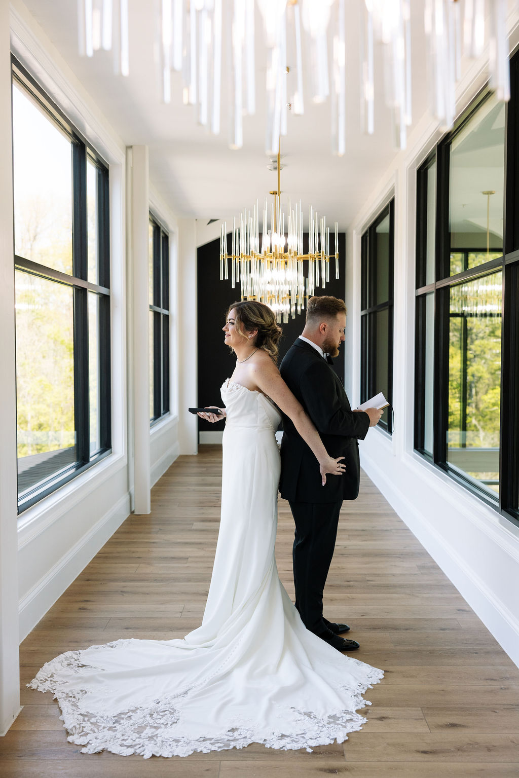 Bride and groom standing back to back reading private vows in bright hallway at a nichols heir wedding