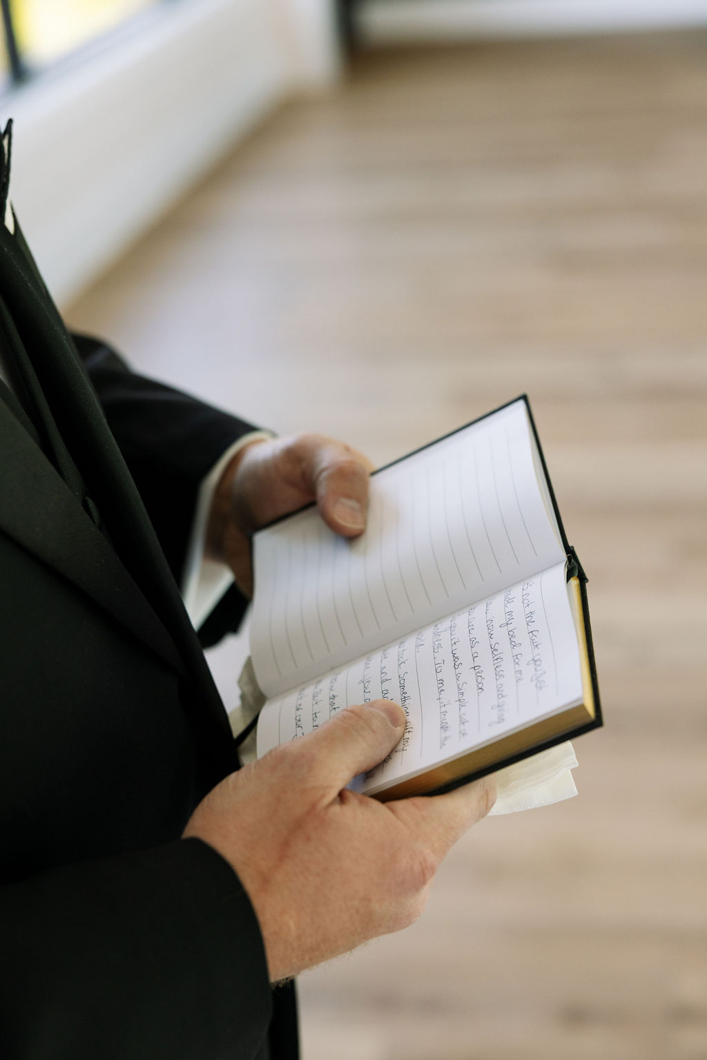 Groom holding handwritten vows in notebook, quiet getting ready detail before ceremony