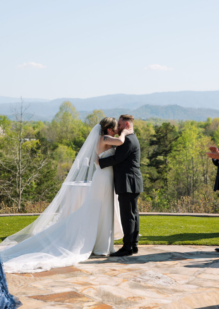 Bride and groom sharing their first kiss at ceremony with scenic overlook backdrop