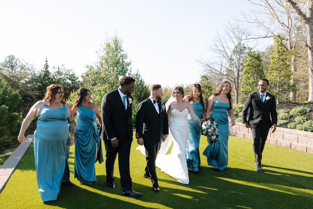 Wedding party walking together on lawn in coordinated blue dresses and black suits during a nichols heir wedding