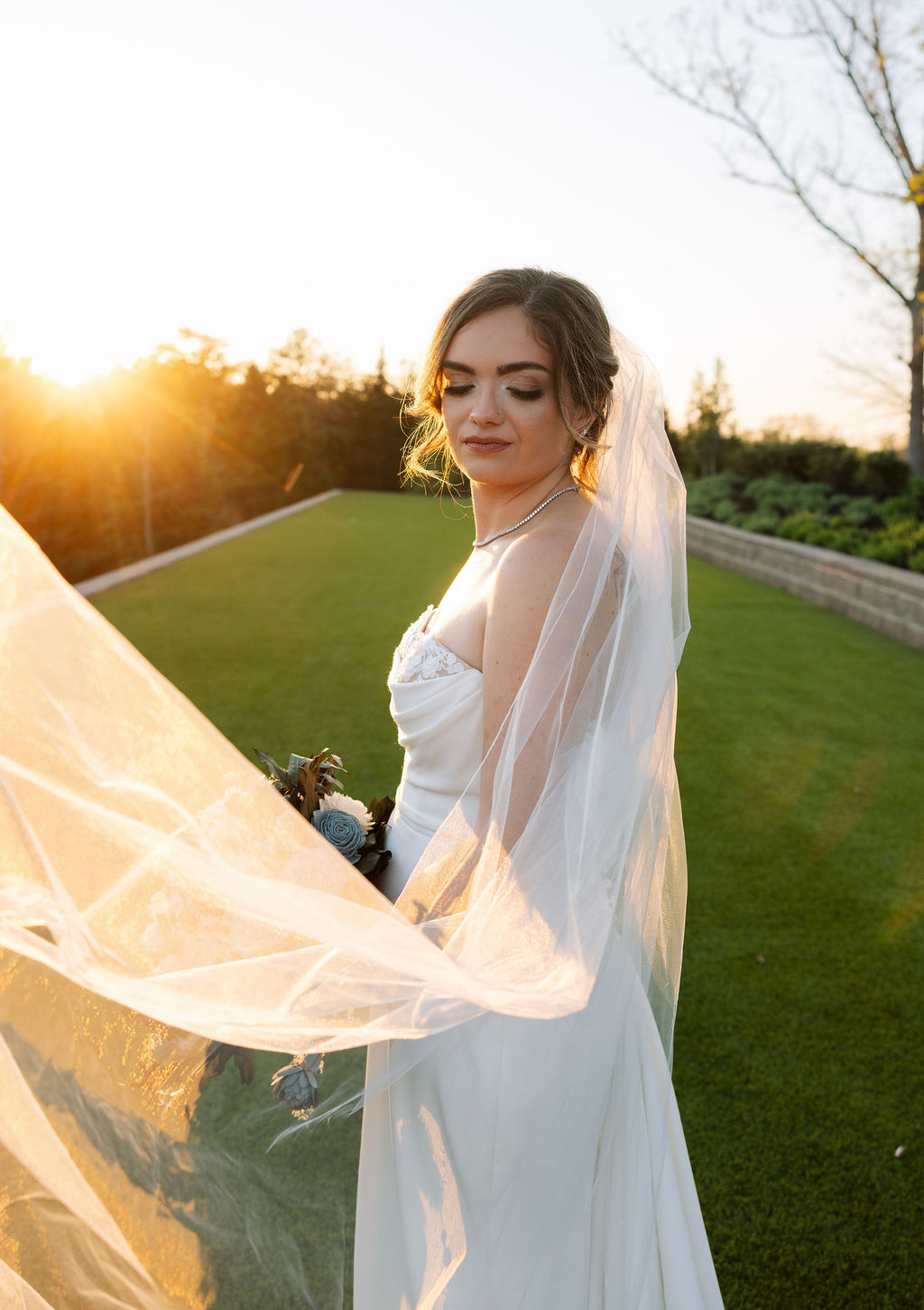 Bride in soft golden hour light with veil movement and bouquet detail at a nichols heir wedding