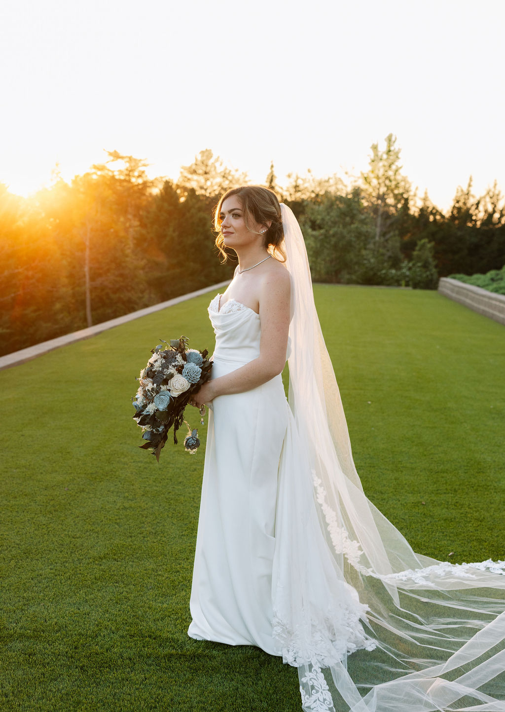 Bride standing in golden hour light holding bouquet on lawn at a nichols heir wedding
