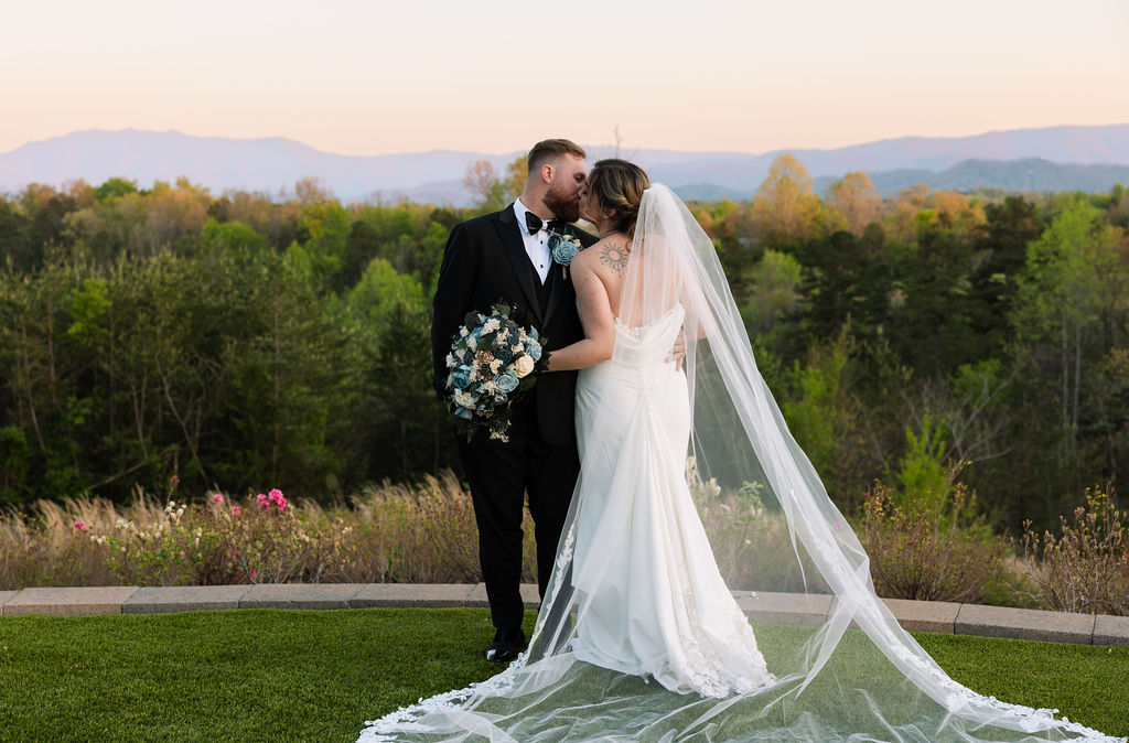 Bride and groom kissing at sunset with mountain views and flowing veil during a nichols heir wedding