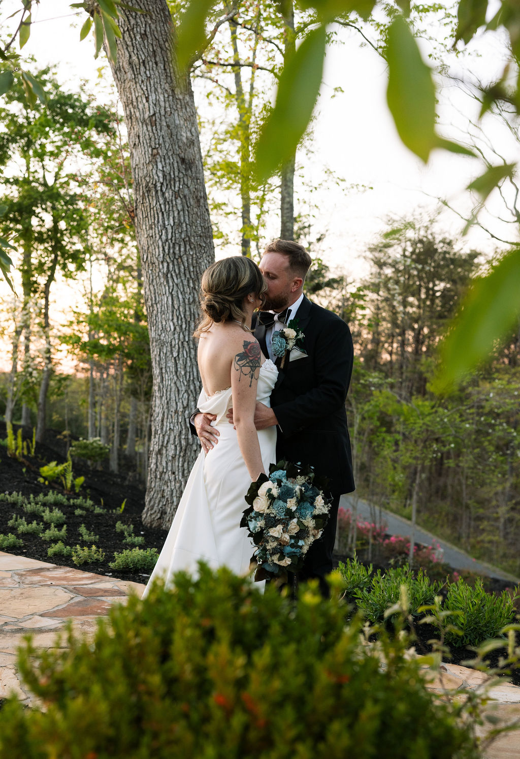 Bride and groom sharing a kiss surrounded by greenery during golden hour portraits at a nichols heir wedding