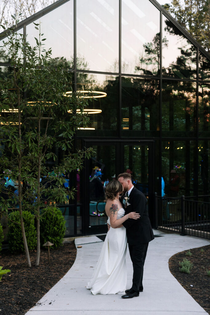 Bride and groom standing outside modern glass venue at dusk with reflections and soft lighting during a nichols heir wedding