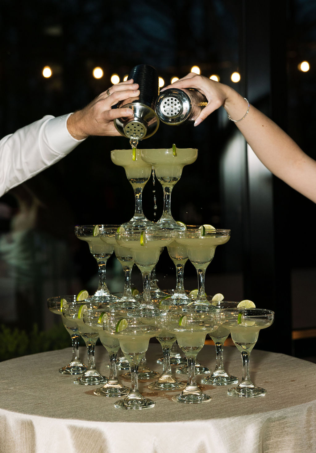 Hands pouring margaritas into stacked glasses, interactive drink display moment