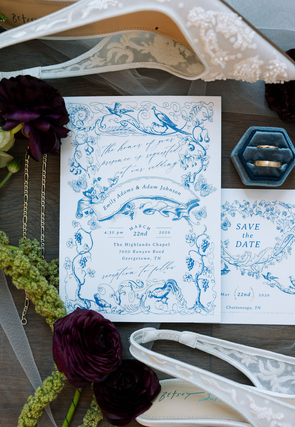 Wedding invitation flat lay with blue ornate details, florals, and bridal accessories