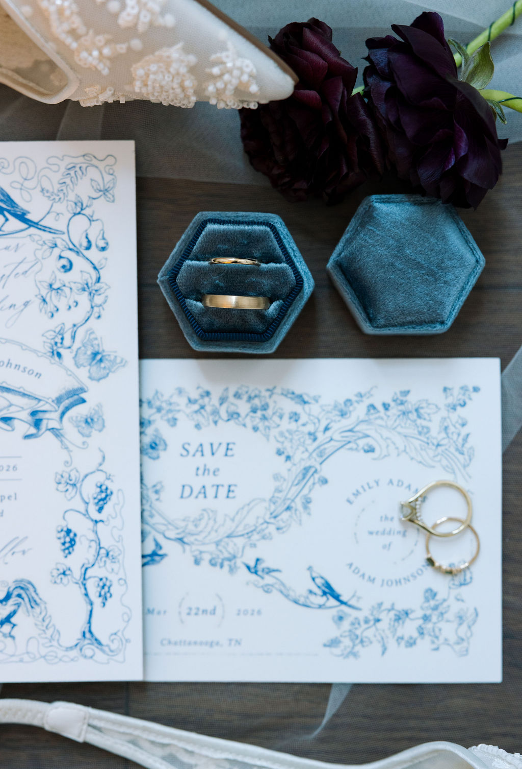 Wedding invitation suite with blue floral design, rings, and velvet ring boxes