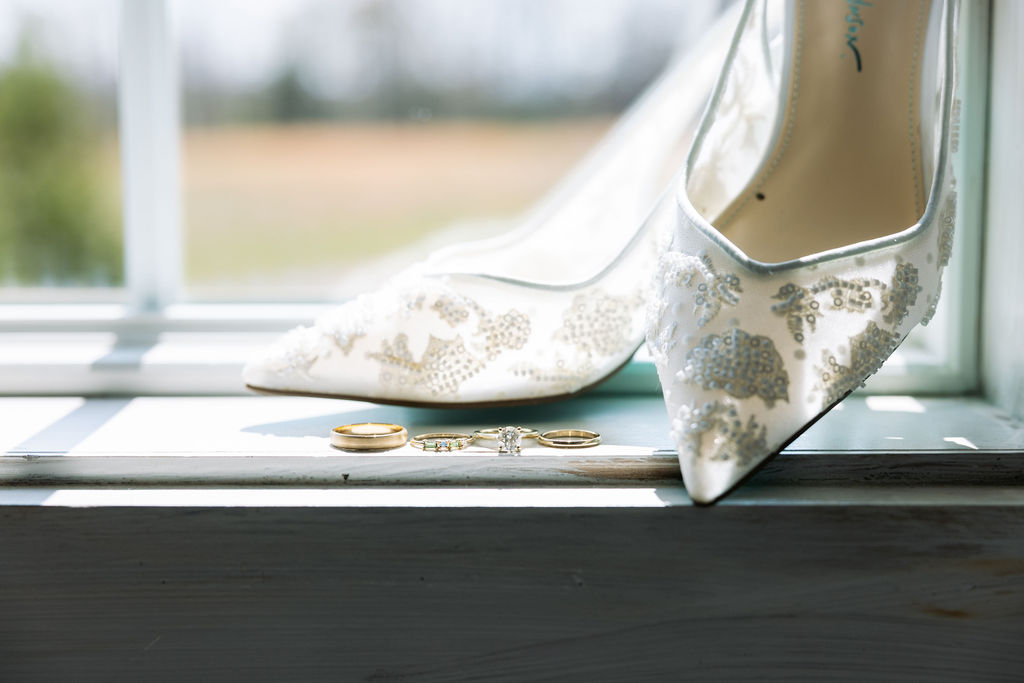 Bridal shoes and wedding rings placed on a windowsill with soft natural light
