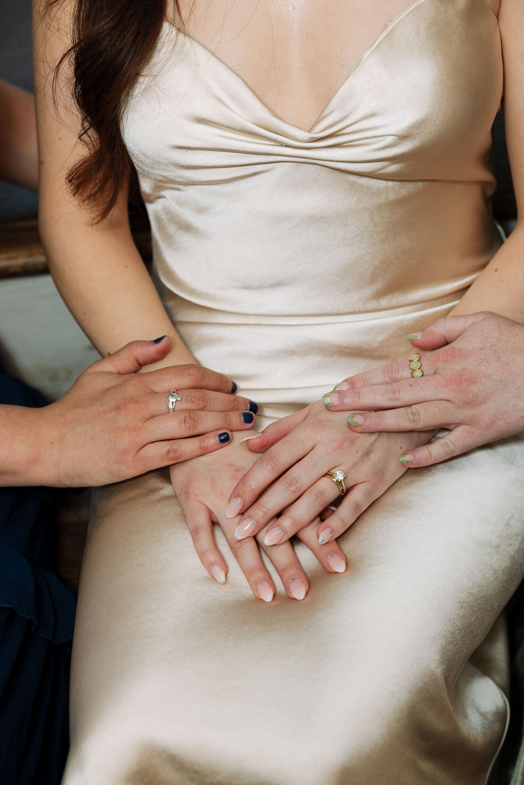 Close-up of bride’s hands with wedding ring as friends gently hold them