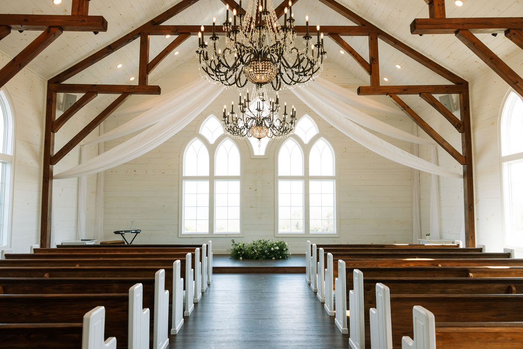 Bright chapel interior with wooden beams, chandeliers, and rows of pews at Howe Farms wedding venue