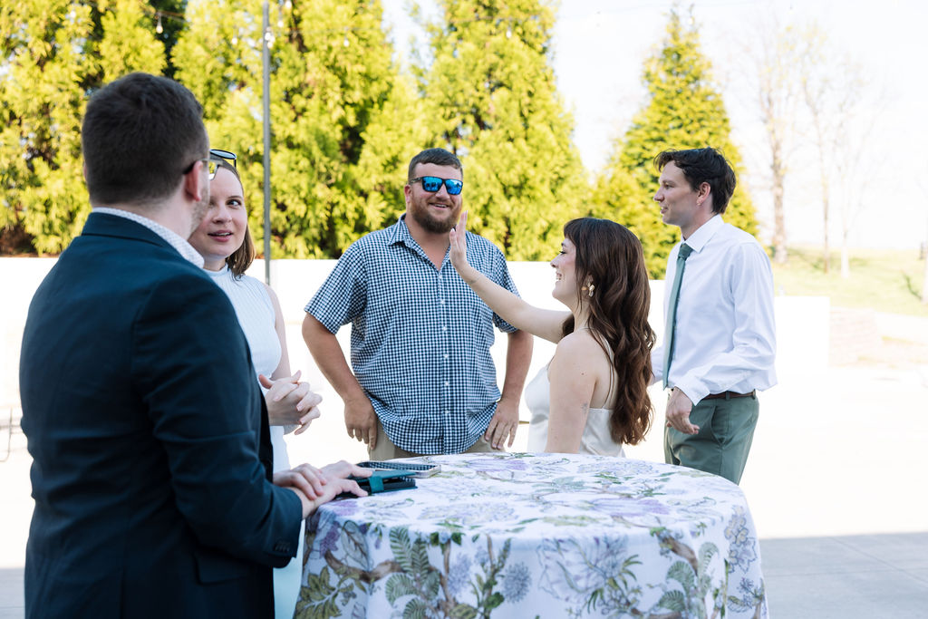 Guests gathered around a table laughing and talking during cocktail hour at Howe Farms wedding venue