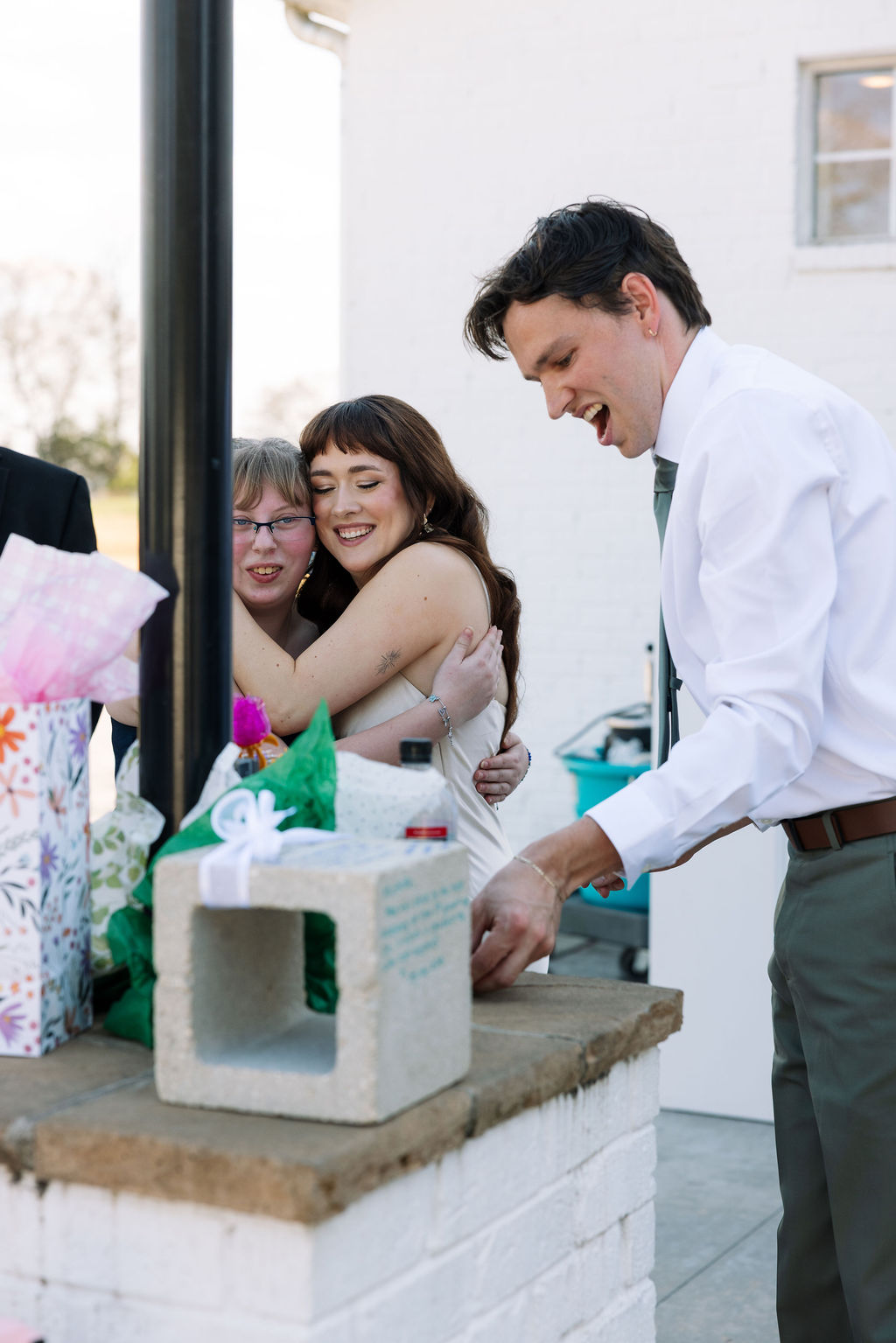 Bride hugging a guest during cocktail hour while the groom opens a gift nearby