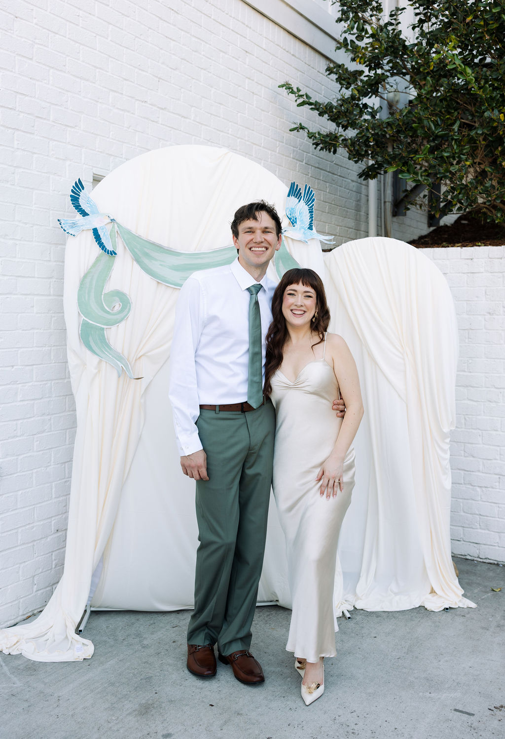 Bride and groom posing together in front of a draped backdrop with soft blue accents