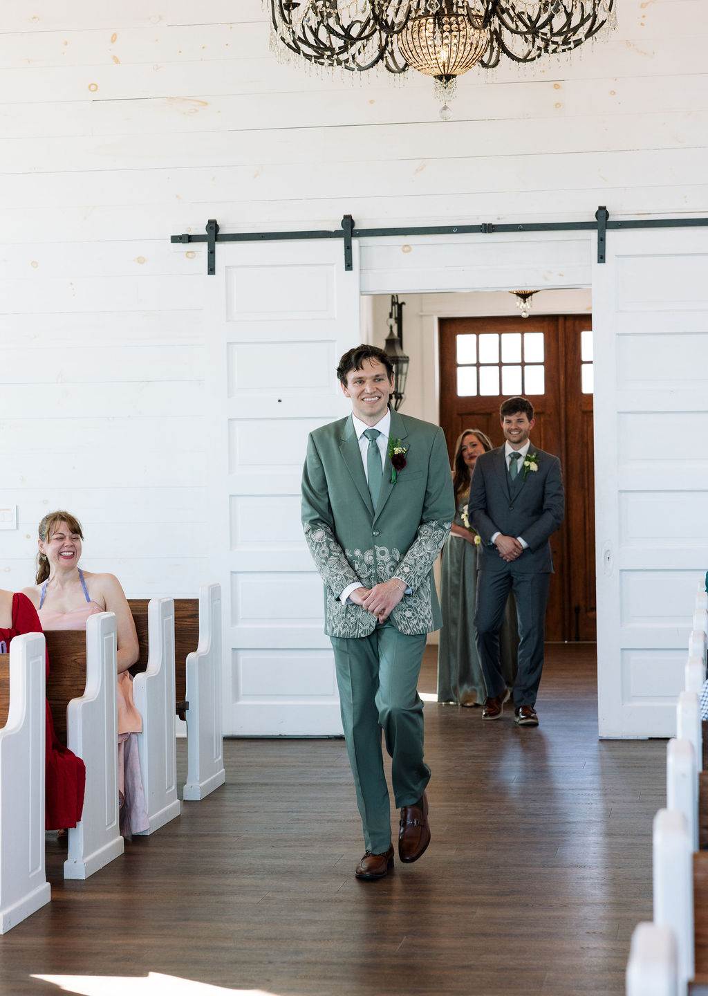 Groom walking down the aisle inside a bright chapel with guests seated on either side
