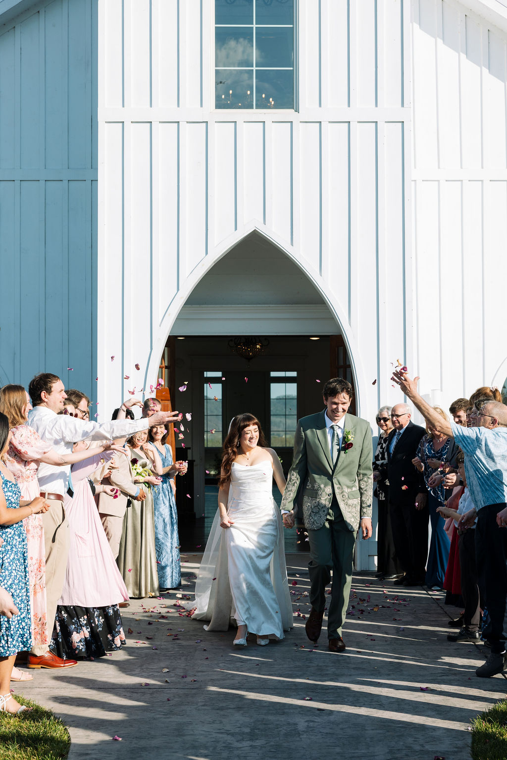 Newlyweds walking out of the chapel as guests toss flower petals at Howe Farms wedding venue