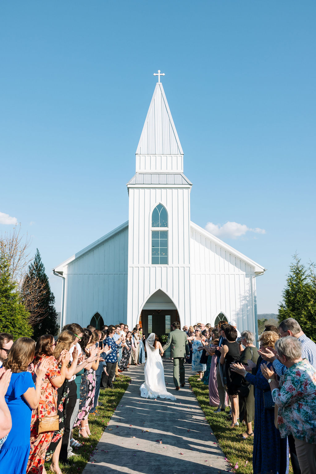 Newlyweds walking away from the chapel as guests line the aisle at Howe Farms wedding venue