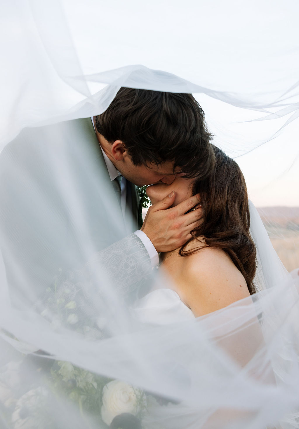 Couple kissing beneath the bride’s veil in a soft, intimate portrait