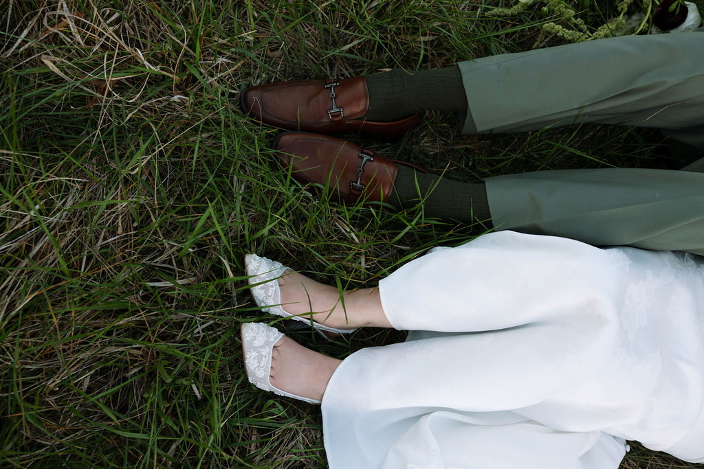 Bride and groom lying side by side in the grass, showing their shoes and wedding attire