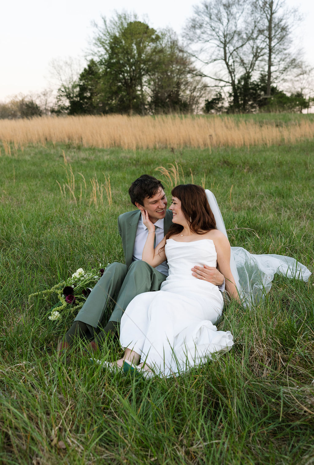 Newlyweds sitting together in tall grass, sharing a quiet moment after their ceremony