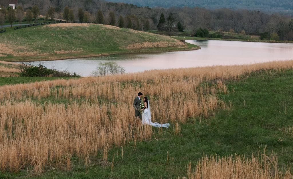 Bride and groom standing together in tall grass overlooking the water