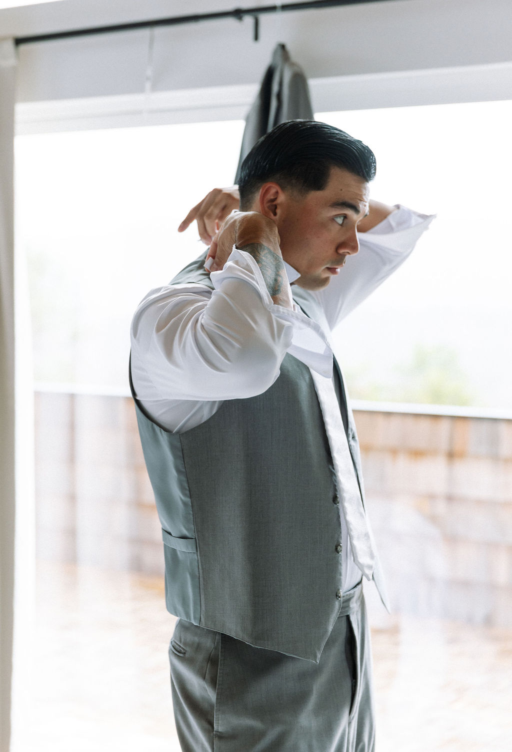 Groom fastening his vest near a window inside The Magnolia Wedding Venue, preparing for the ceremony