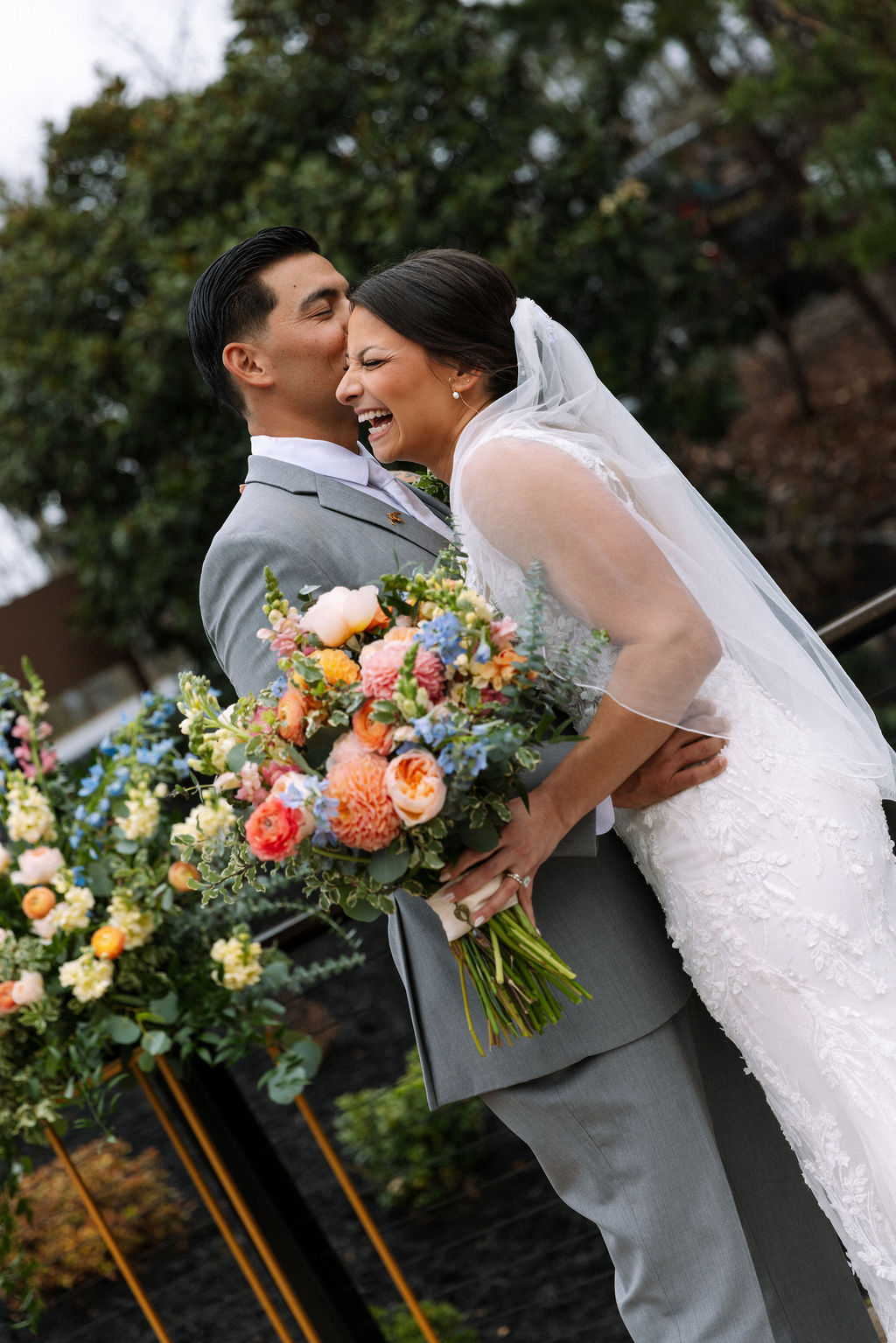 Close-up of bride and groom laughing together with bouquet on a rainy wedding day
