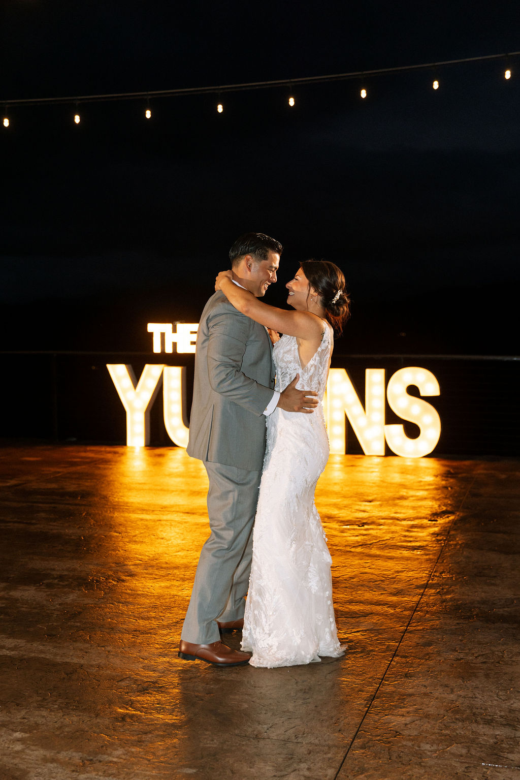 Bride and groom share a quiet first dance at The Magnolia Wedding Venue under string lights and glowing marquee letters
