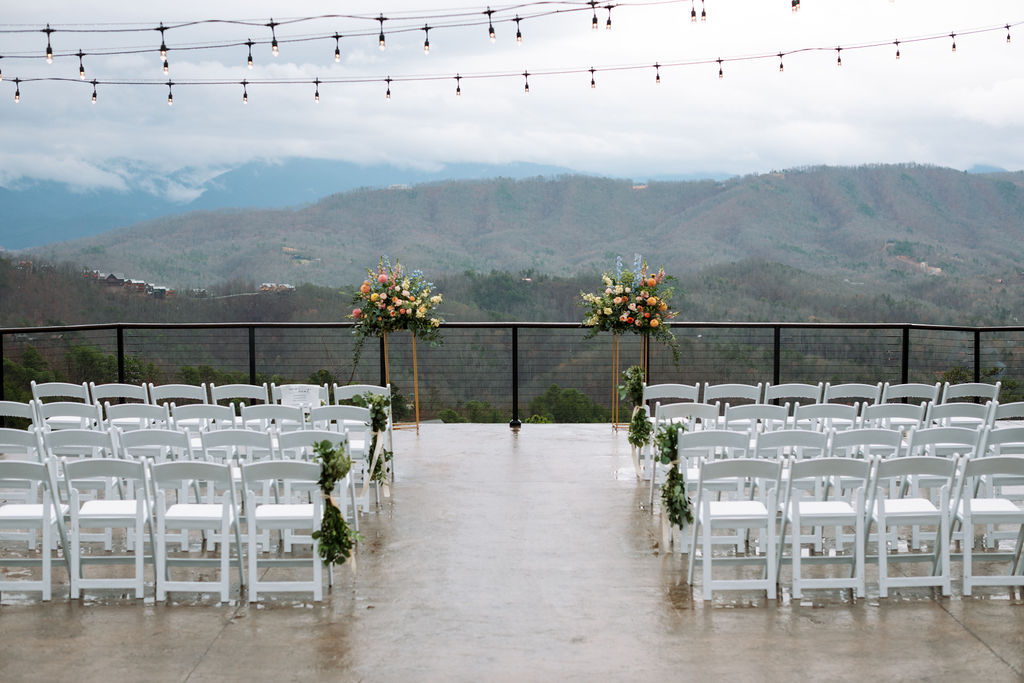 Outdoor ceremony setup at The Magnolia Wedding Venue with white chairs, floral arrangements, and mountain views on a misty day
